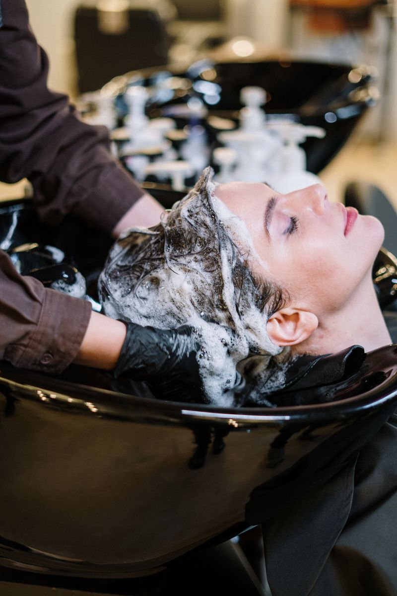 Manos de peluquera aplicando producto decolorante sobre un mechón de cabello claro